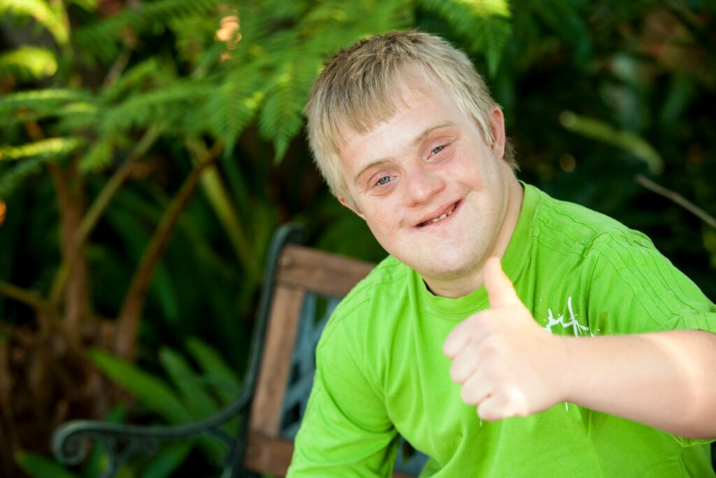 Smiling teenaged boy with Down synrdome giving the thumbs up