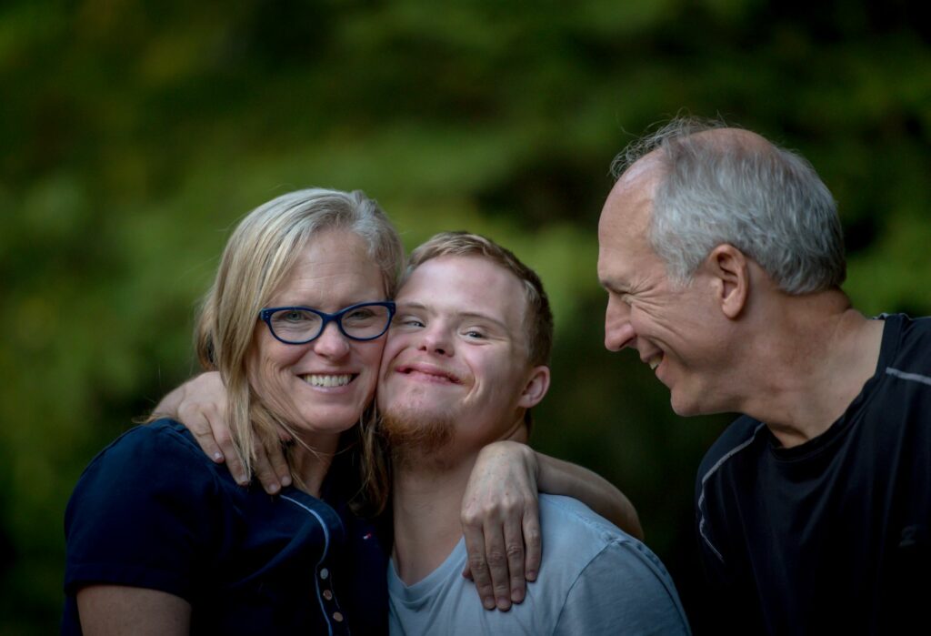 A smiling middle aged couple sharing a happy moment with a teenaged boy. The teenager has his arm around the woman's shoulders and is pressing his cheek to her face.