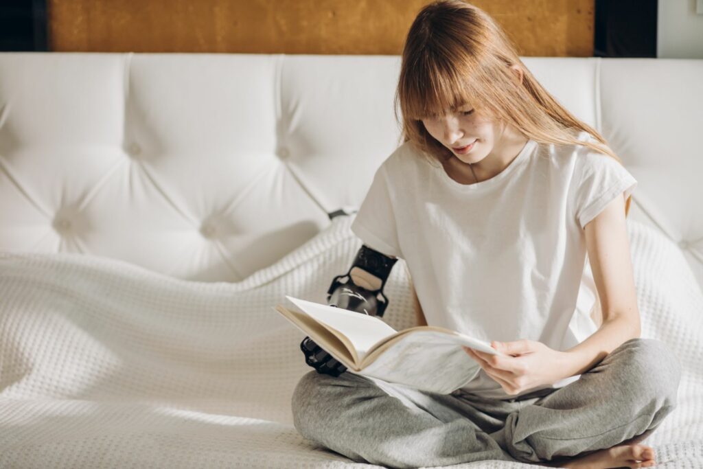 A young woman sitting cross-legged on a bed reading a book.