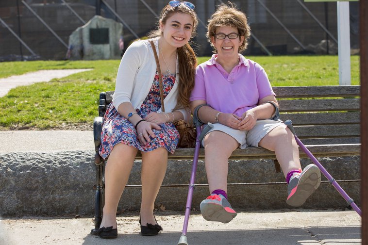 Woman with cerebral palsy sitting with another woman on a a park bench